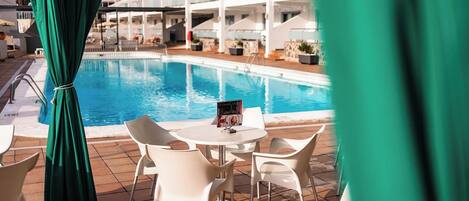 A poolside area with a table and chairs, a brochure, and a view of a hotel building in the background.