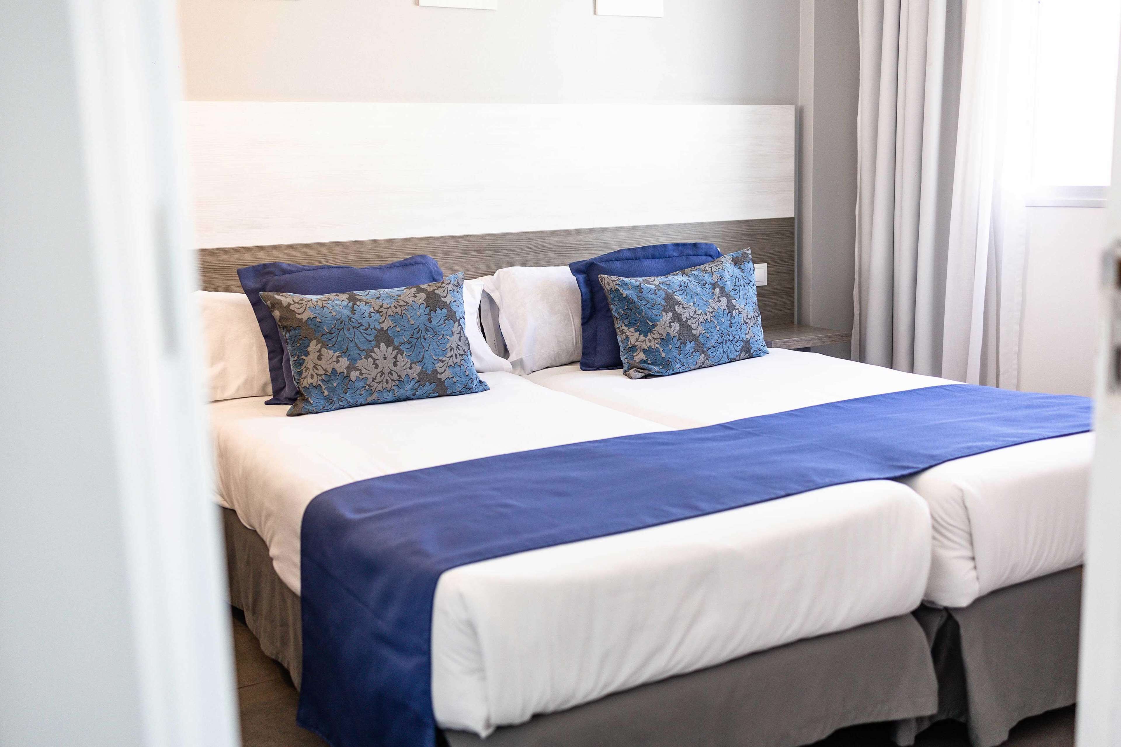 A double bed with a white and blue bedspread, two decorative pillows, and a wooden headboard.