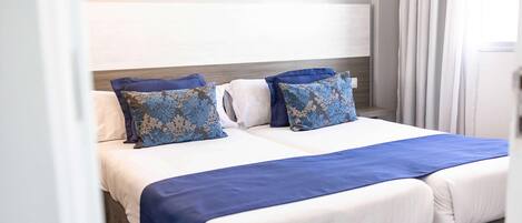 A double bed with a white and blue bedspread, two decorative pillows, and a wooden headboard.