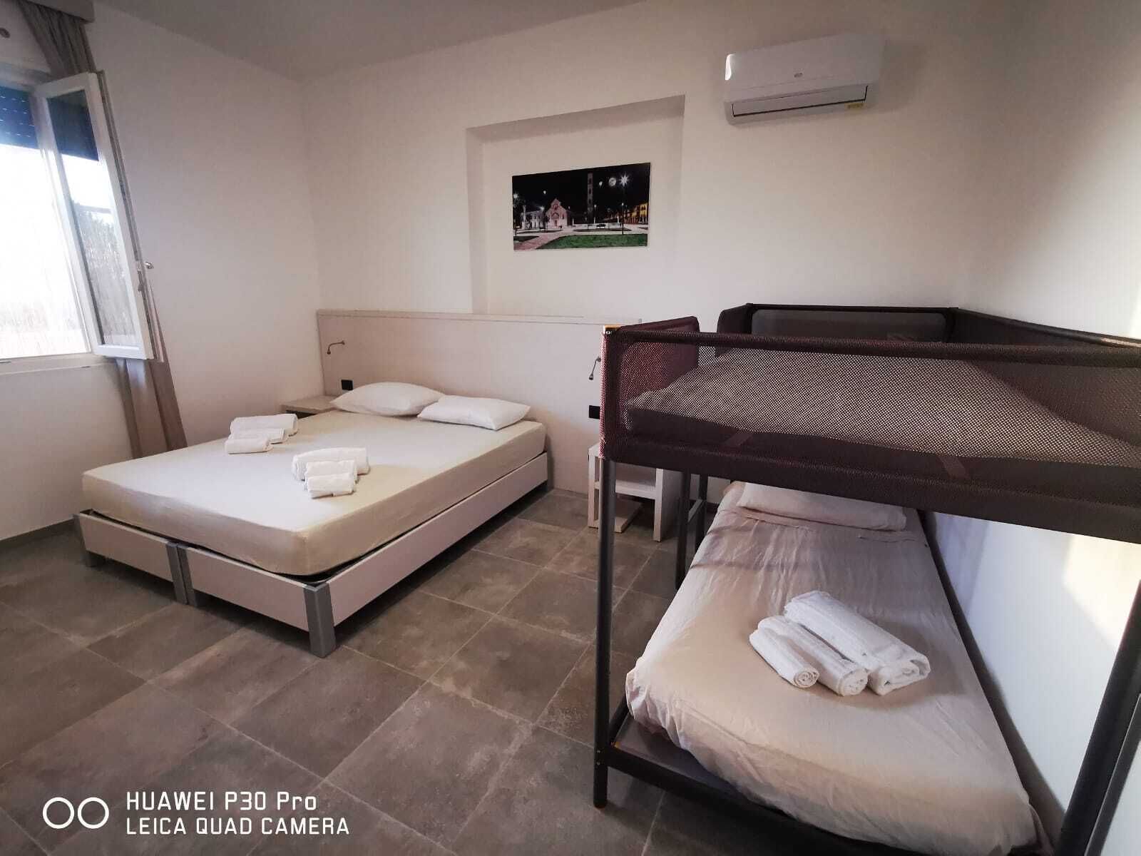 Une chambre d’hôtel avec un lit, un lit superposé, une fenêtre, un climatiseur et un tableau encadré au mur.