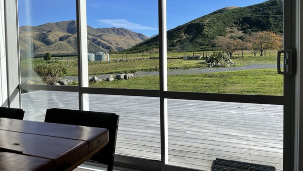 A room with a large window overlooking a grassy landscape with mountains and a fence. - Pudding Hill Lodge & Chalets (Methven)
