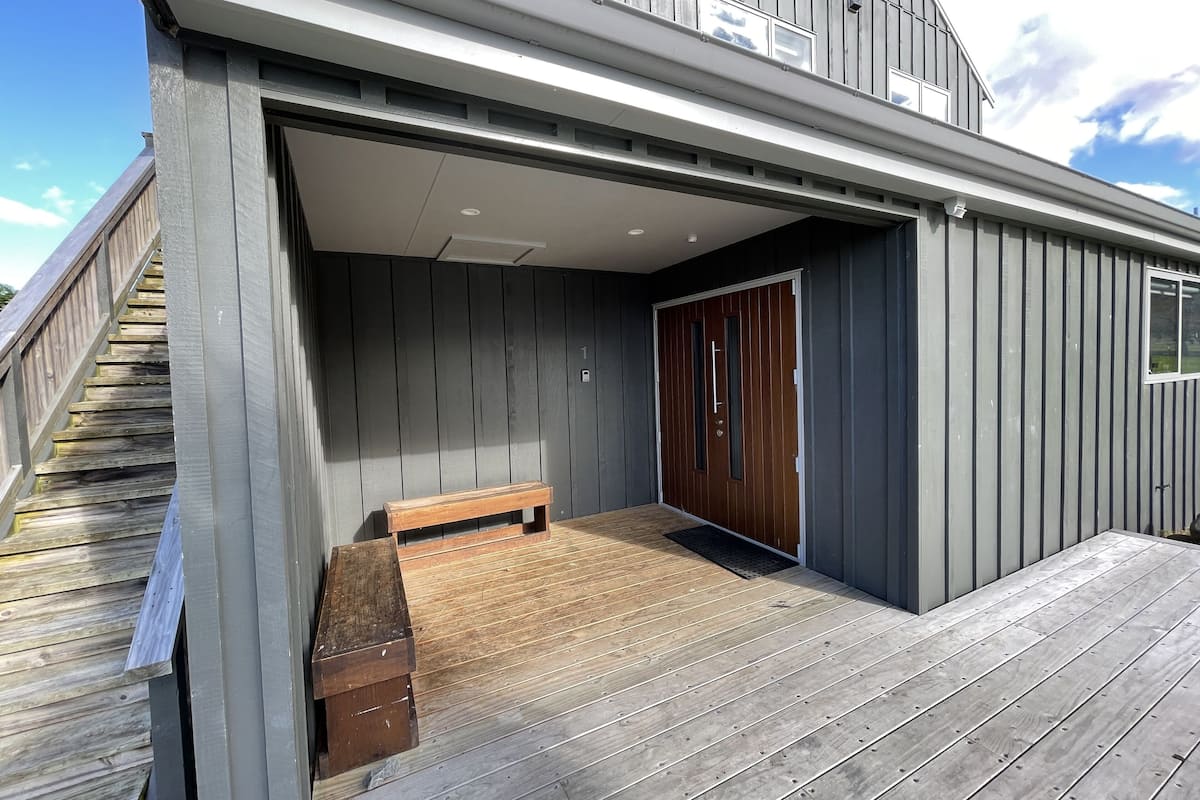 A covered outdoor area with a wooden bench, a door, and a staircase leading to an upper level.