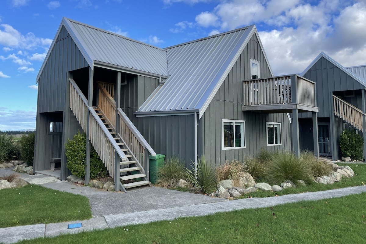 A modern two-story house with a metal roof, a wooden staircase, and a balcony.