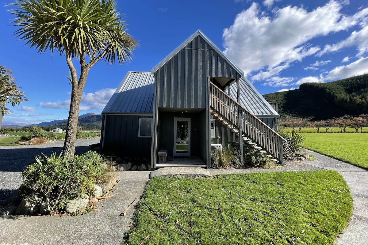 A modern building with a metal roof, a wooden staircase, and a well-maintained lawn.