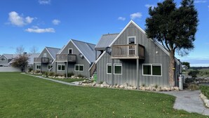 A row of modern, grey houses with balconies, a well-maintained lawn, and a clear blue sky. - Pudding Hill Lodge & Chalets (Methven)