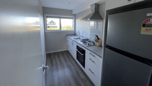 A compact kitchen with a gas stove, sink, and a stainless steel refrigerator. - Pudding Hill Lodge & Chalets (Methven)
