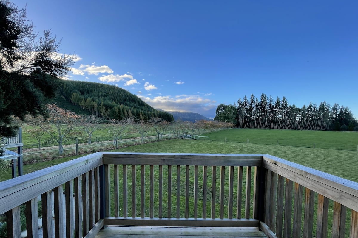A wooden deck with a view of a grassy field and trees.