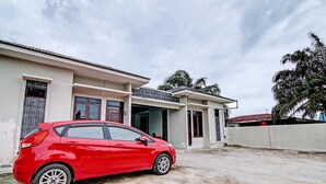 A red car parked in front of a building with a flat roof and a concrete ground. - Hotel O Sandira Syariah (Dumai)