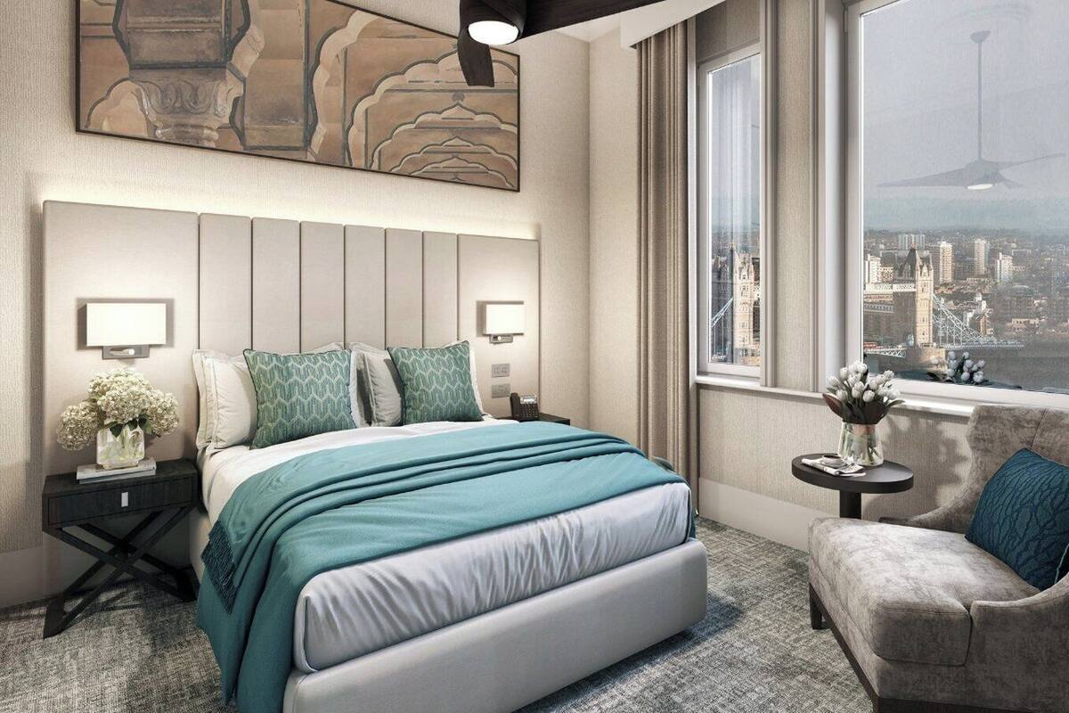 A modern hotel room with a large bed, a city view, a small side table, and a comfortable armchair.