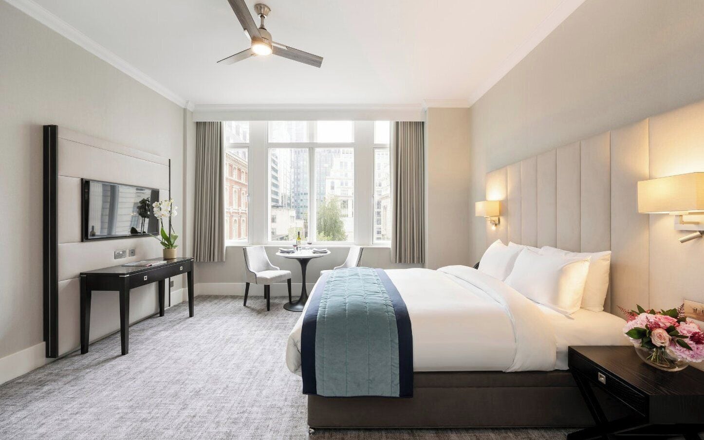 A hotel room with a bed, a desk, a chair, a TV, and a window with a city view.