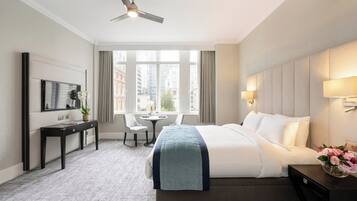 A hotel room with a bed, a desk, a chair, a TV, and a window with a city view.