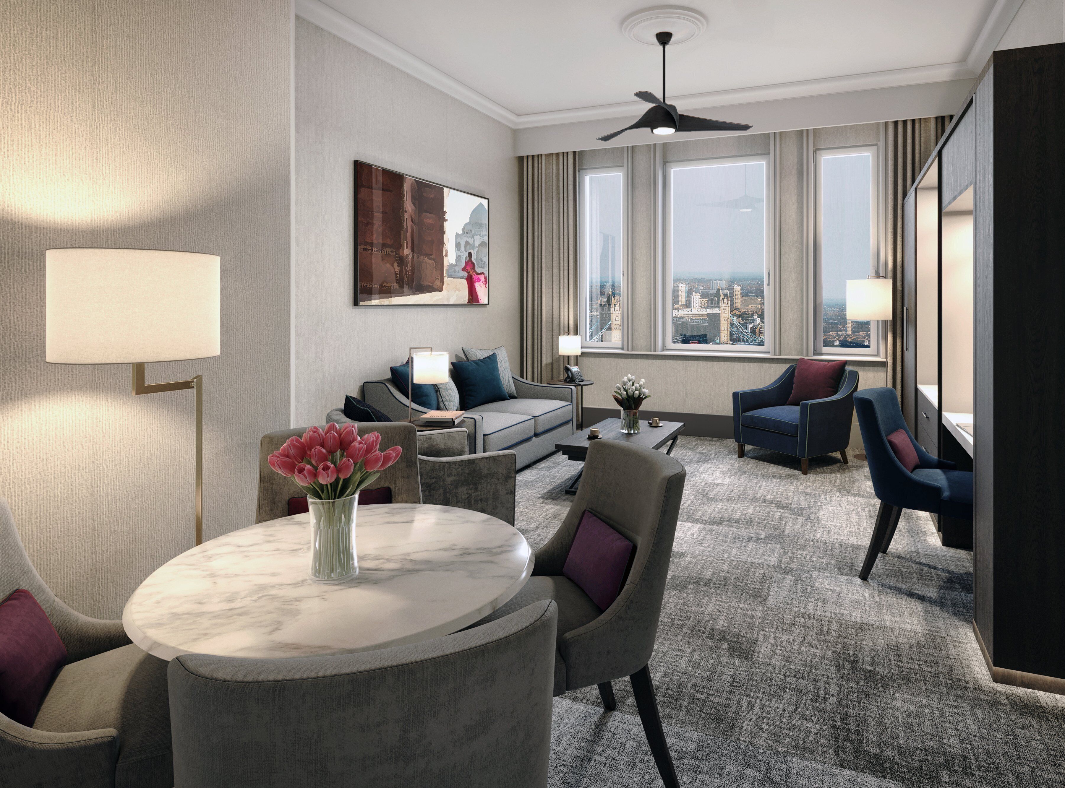 Habitación de hotel con vista a la ciudad, un sofá, una mesa de comedor con un jarrón de flores y un ventilador de techo.