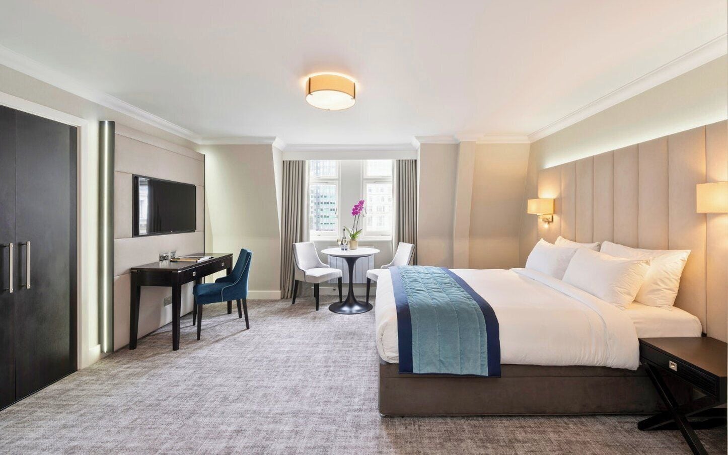 Une chambre d’hôtel équipée d’un lit, d’un bureau, d’une chaise, d’une petite table et d’un téléviseur.