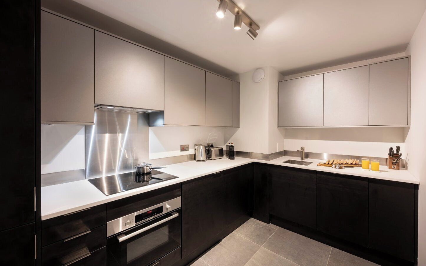 Een moderne keuken met zwarte kastjes, roestvrijstalen apparatuur en een wit aanrecht.