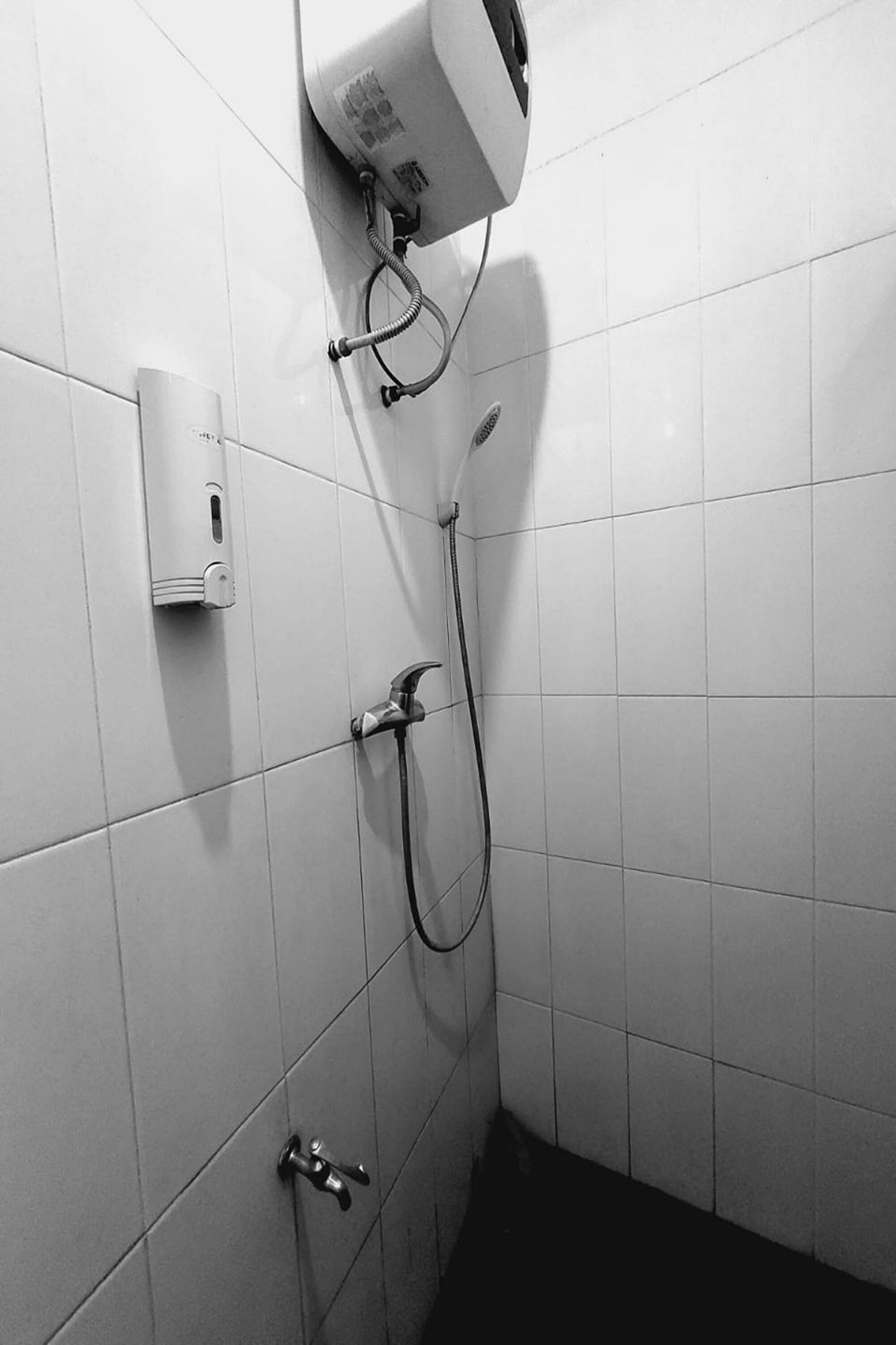 Baño con paredes de azulejos blancos, cabezal de ducha manual y grifo empotrado.