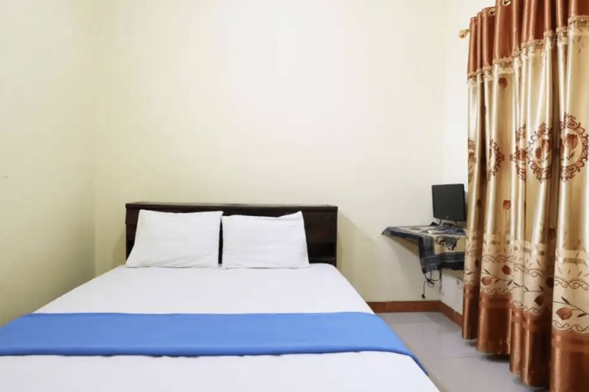 A neatly made bed with white and blue bedding, a wooden headboard, and a desk with a computer and a chair.