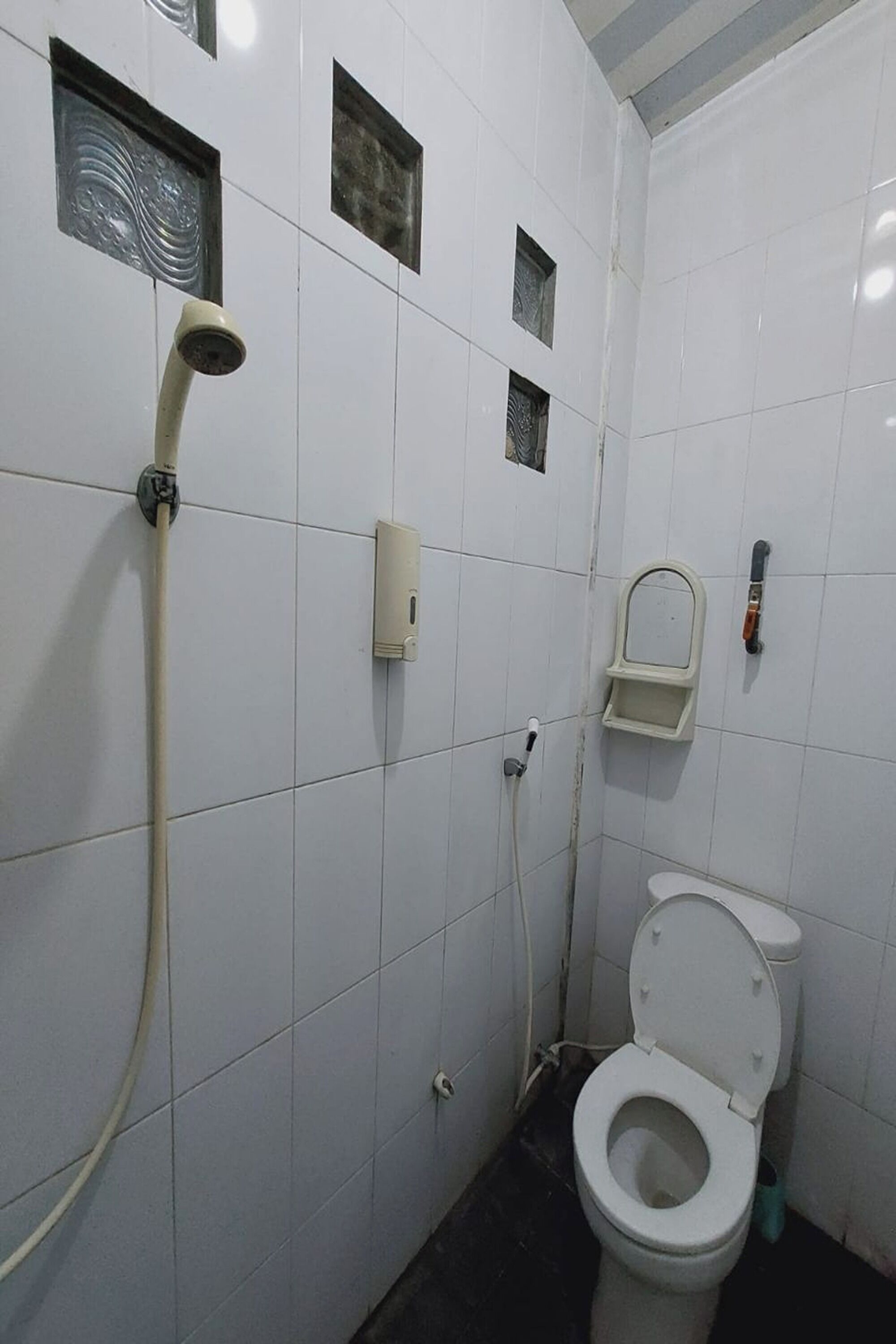 A small, tiled bathroom with a toilet, a shower, and a soap dispenser.