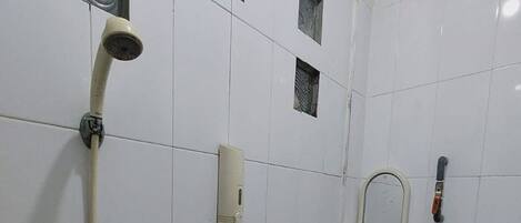 A small, tiled bathroom with a toilet, a shower, and a soap dispenser.