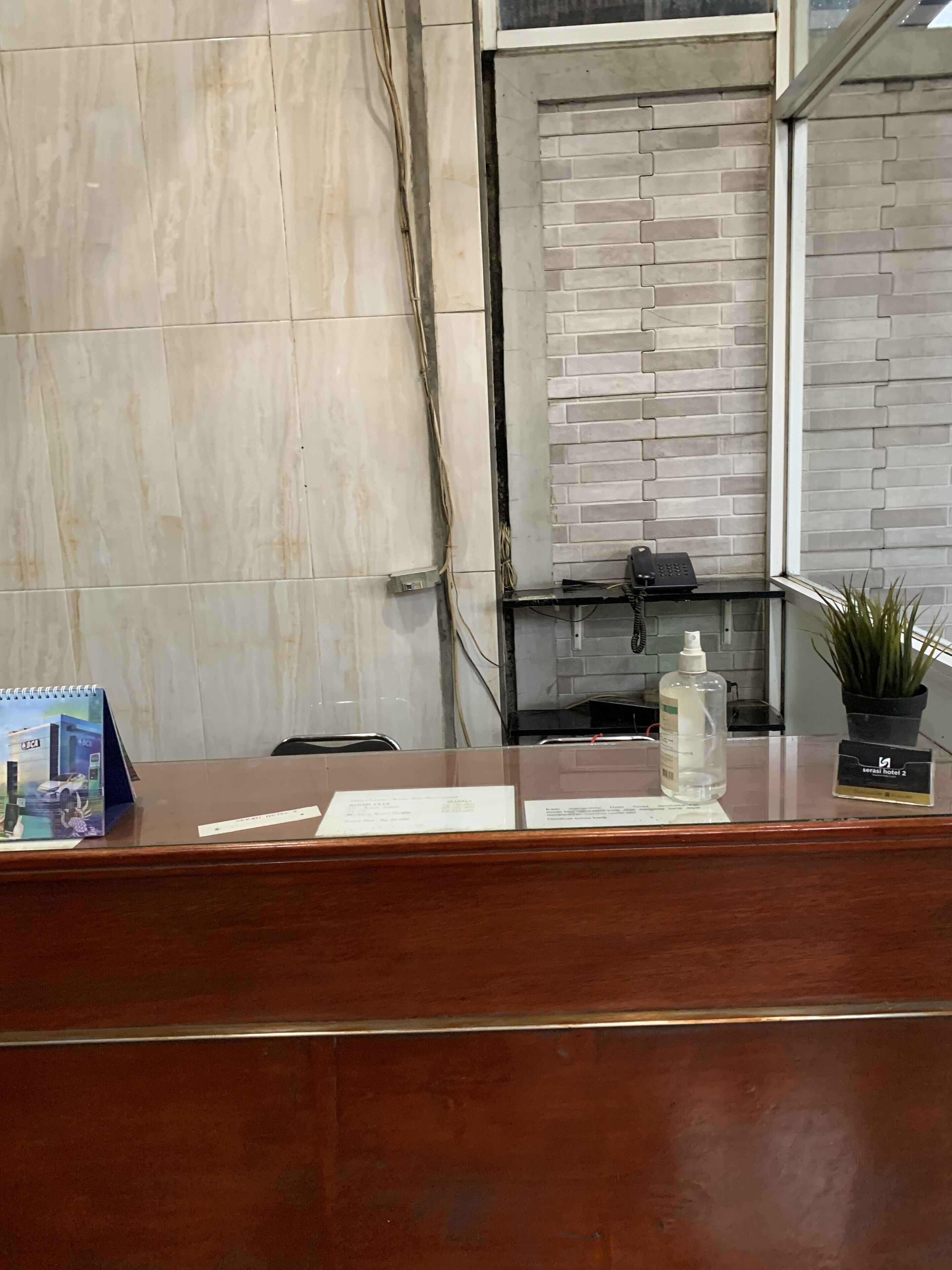 Un comptoir d’accueil d’hôtel en bois, avec un téléphone, une plante et une bouteille d’eau.