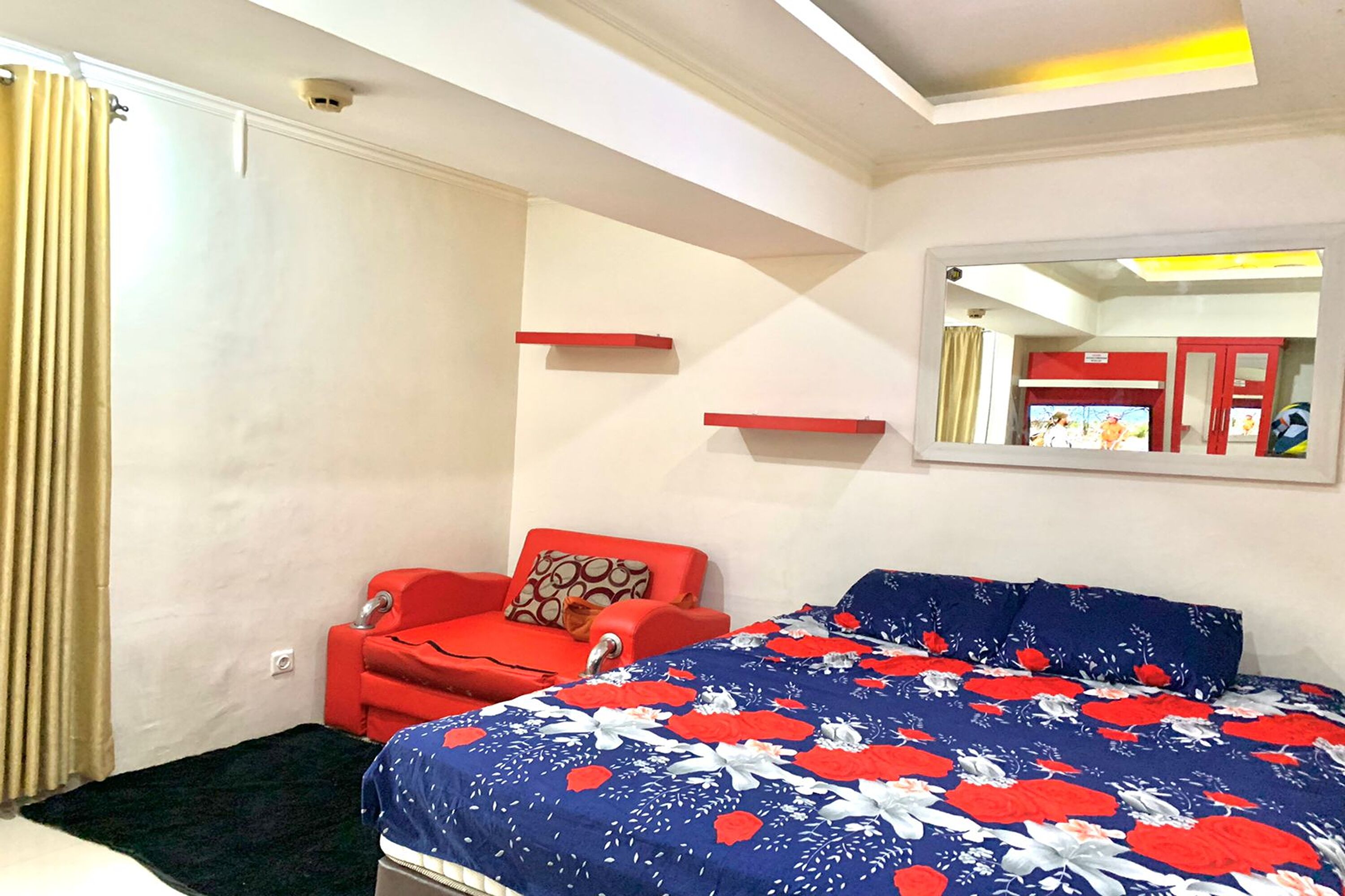 Quarto com uma cama, uma cadeira vermelha, um espelho e uma estante vermelha.