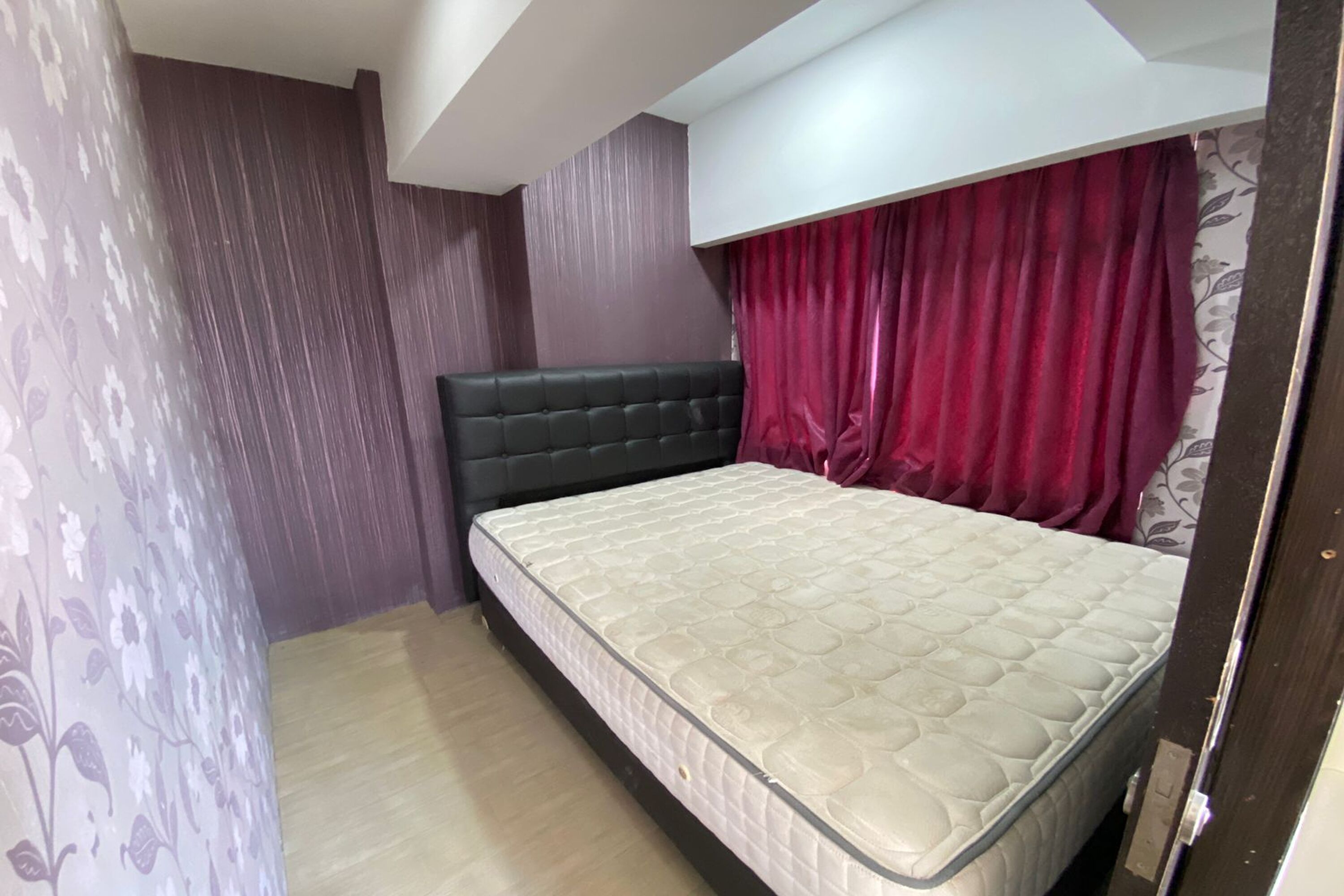 A bedroom with a bed, dark headboard, and red curtains.
