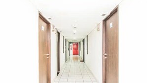 A long, narrow hallway with wooden doors on either side and a tiled floor. - Cozy Room @ Hallo Tidur By Tio (Bandung)