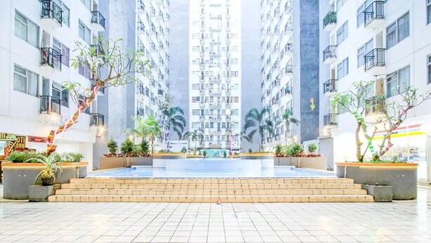A modern hotel atrium with high-rise buildings, a central fountain, and potted plants. - Cozy Room @ Hallo Tidur By Tio (Bandung)