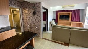 A modern living room with a sofa, a TV, and a kitchen area with a countertop. - Cozy Room @ Hallo Tidur By Tio (Bandung)