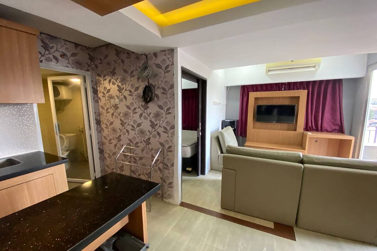 Een moderne woonruimte met een bank, een flatscreen televisie en een keuken met een aanrecht en kastjes.