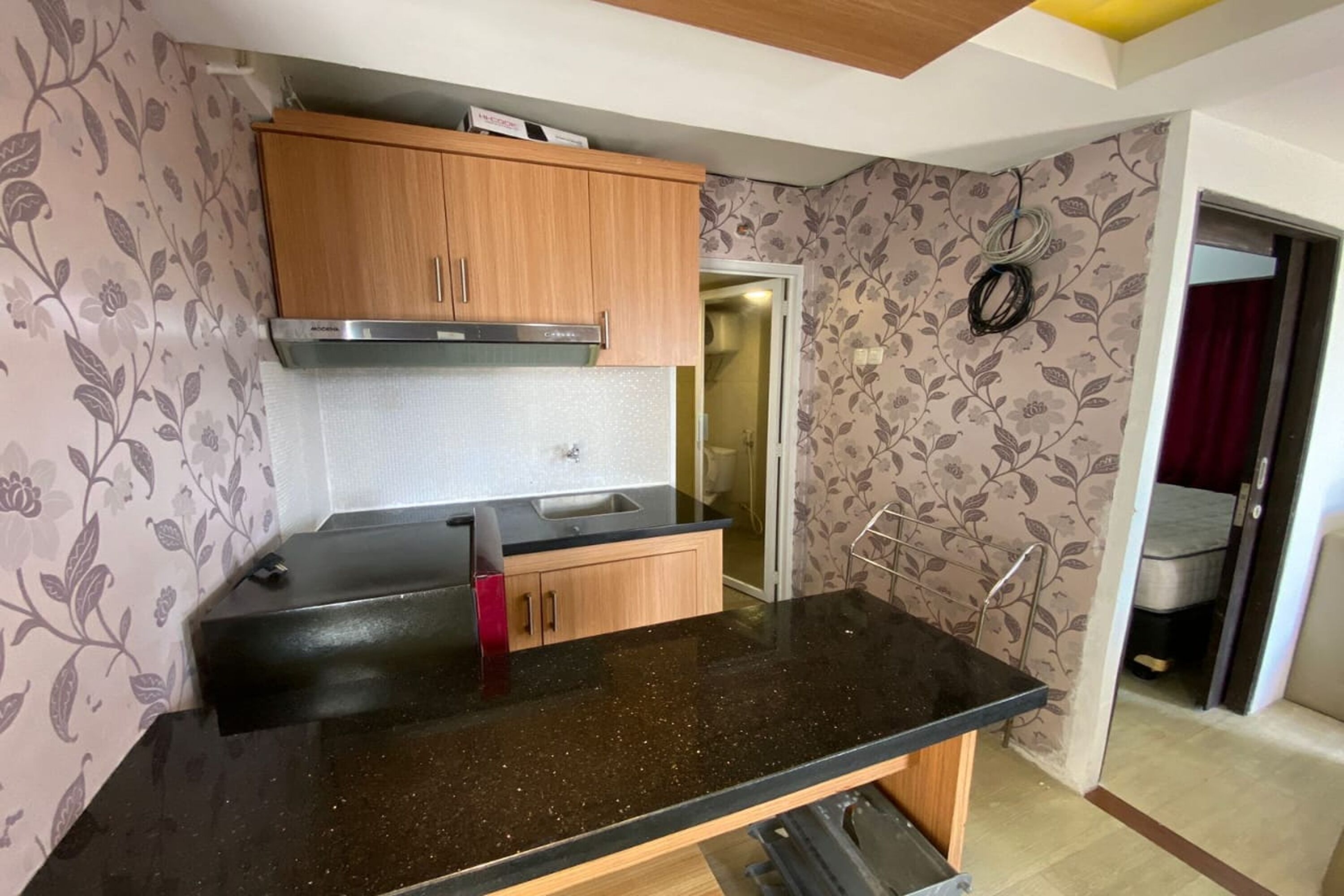 A compact kitchen with wooden cabinets, a black countertop, and a stainless steel range hood.