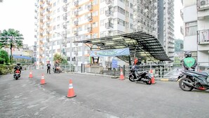 A multi-story residential building with balconies, a covered outdoor seating area, and traffic cones on the street. - Cozy Room @ Hallo Tidur By Tio (Bandung)