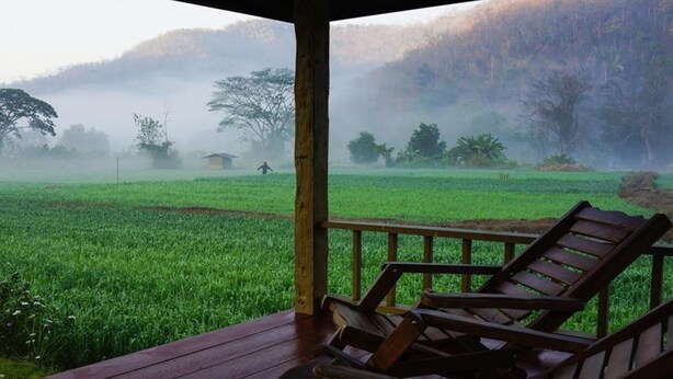 Un pontile in legno con due poltrone a schiacciasassi, vista su un prato verde e una zona boschiva avvolta nella nebbia.
