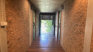 Un corridoio con pareti in mattoni e pavimento in legno conduce a un balcone con vista sugli alberi.