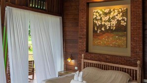 Una camera da letto con un letto di legno, un'ampia finestra con tende bianche, un muro in mattoni e un quadro con fiori.