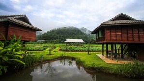 Un edificio tradizionale in legno con tetto di paglia, immerso nel verde e con un piccolo stagno.