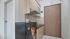 A compact kitchen with a black refrigerator, wooden cabinets, a microwave, and a wooden door. - Room Rendi @ Podomoro Golf View (Gunung Putri)