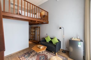 A living room with a sofa, a coffee table, a floor lamp, a bookshelf, and a refrigerator.