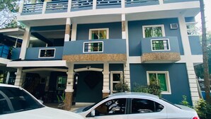 A multi-story building with a balcony, a car parked in front, and a palm tree. - Rachel's Bed and Breakfast Near Tagaytay (Silang)