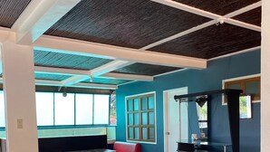 A spacious room with a high ceiling, a red sofa, a wooden table, and a bar area with a cushioned bar stool. - Rachel's Bed and Breakfast Near Tagaytay (Silang)