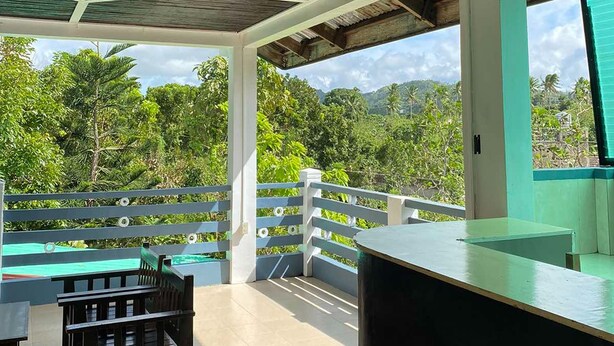 A covered outdoor area with a pool, seating, and a view of the surrounding greenery. - Rachel's Bed and Breakfast Near Tagaytay (Silang)