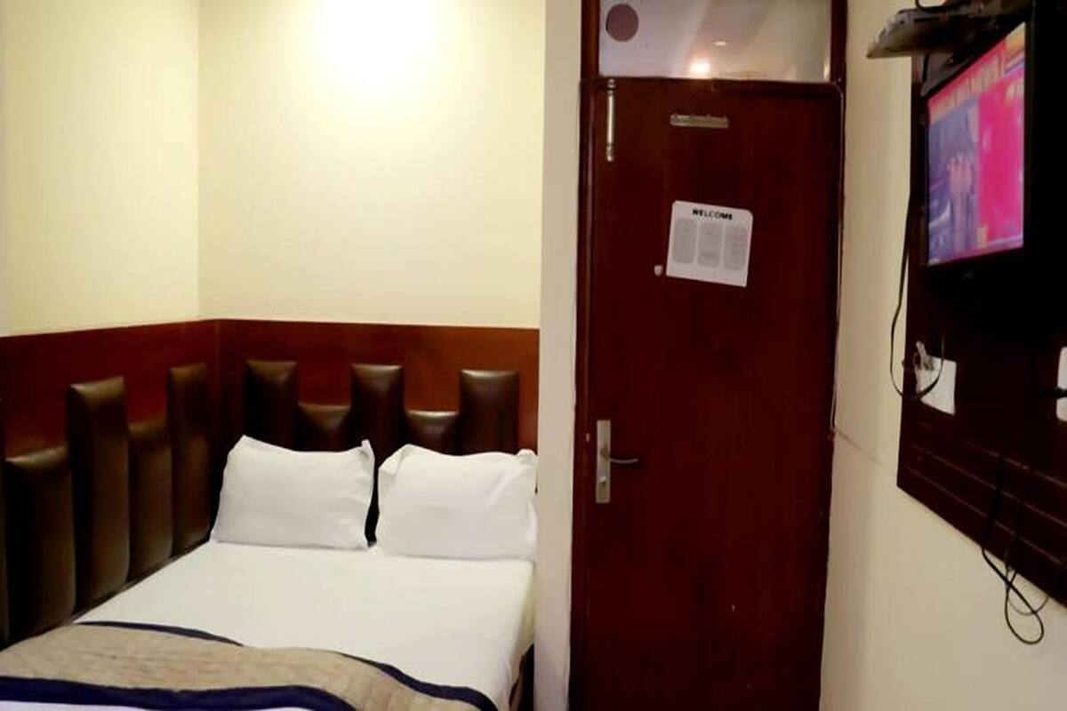 A hotel room with a bed, a wooden headboard, a door with a nameplate, and a television mounted on the wall.