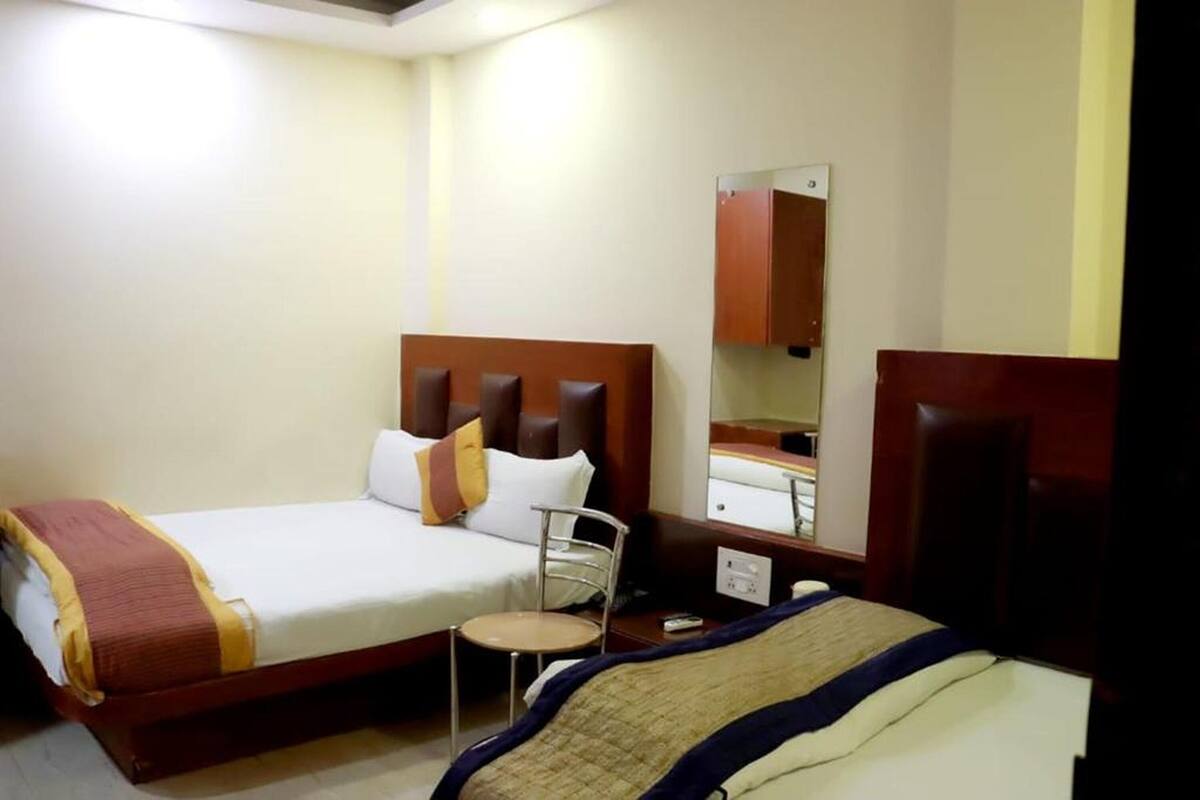 A hotel room with two beds, a small round table, a mirror, and a wooden headboard.