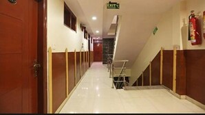 A hotel corridor with wooden doors, an exit sign, and a fire extinguisher on the wall. - Hotel Prem Deluxe Guest House (New Delhi)