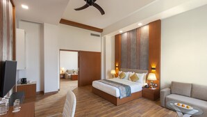 A modern hotel room with a wooden floor, a large bed with a headboard, a TV, a desk, a chair, a sofa, and a ceiling fan. - Clarks Resort Birgunj (Birgunj)