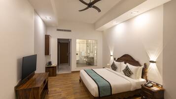 A modern hotel room with a wooden bed, a flat-screen TV, a ceiling fan, and a bathroom visible through a glass door.