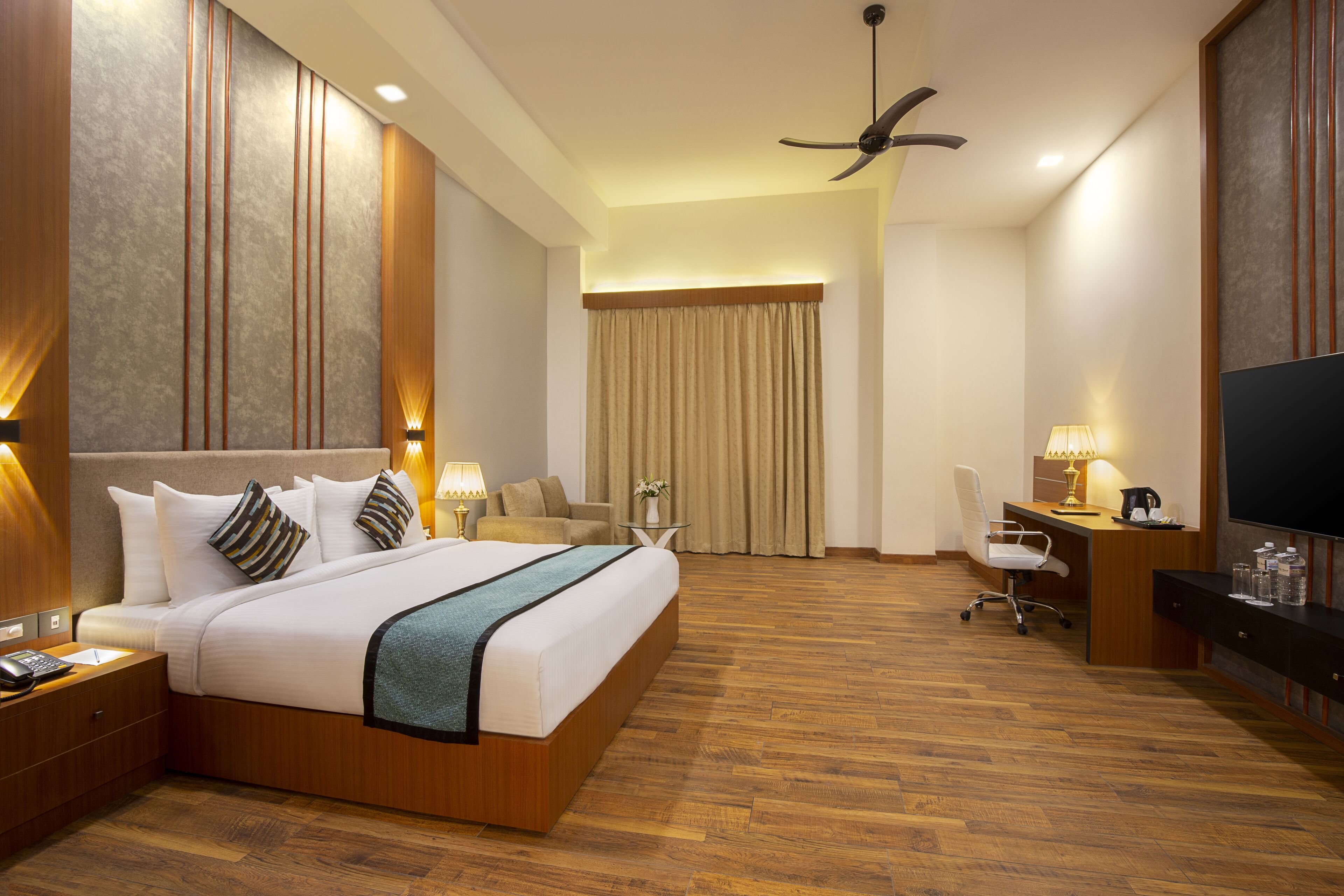A hotel room with a large bed, a desk with a chair, a television, and a ceiling fan.