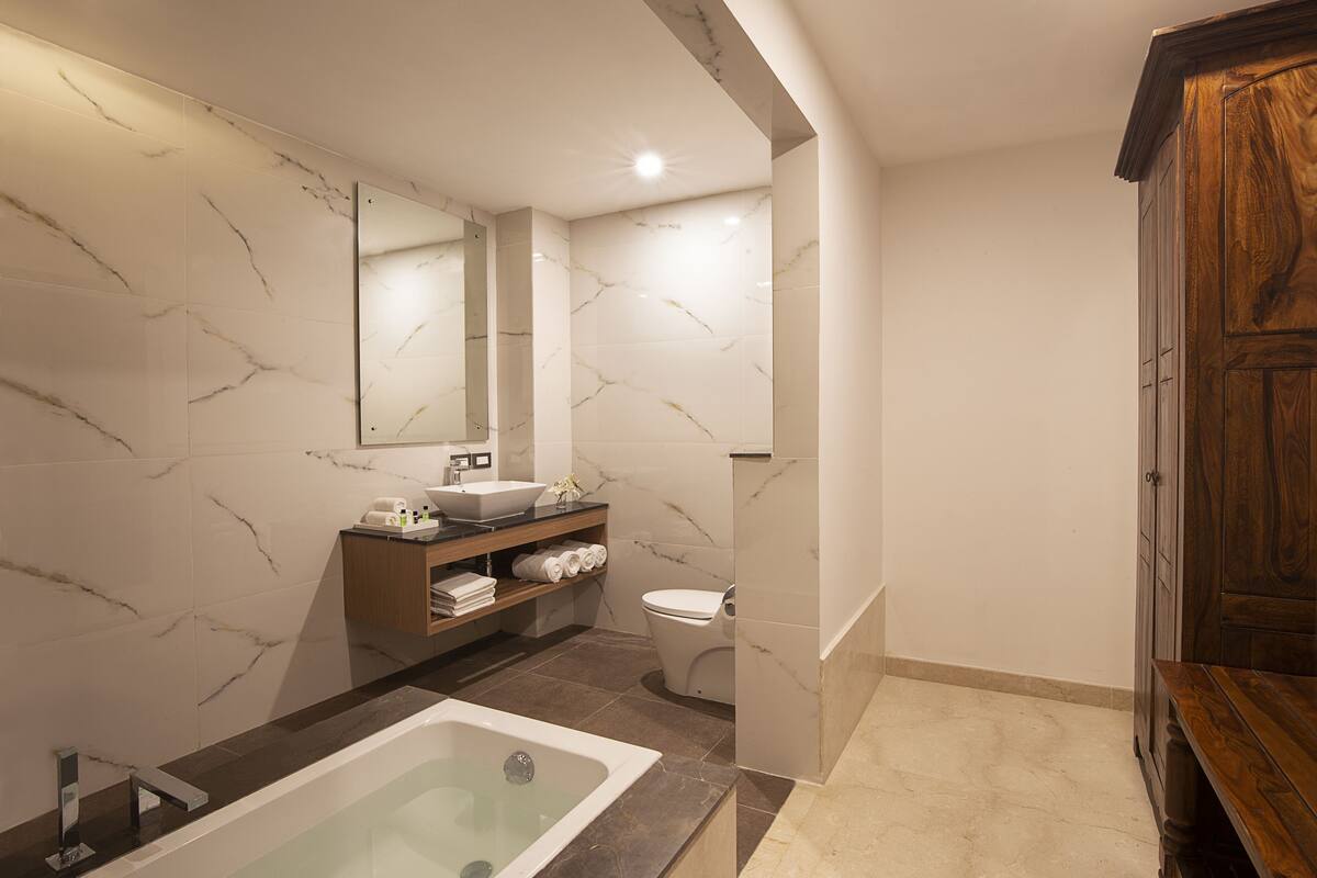A modern bathroom with a marble wall, a bathtub, a sink, and a wooden cabinet.