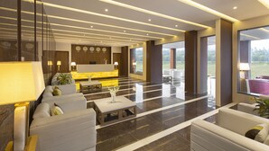 A modern lobby with a reception desk, seating area, and large windows offering a view of the outdoors. - Clarks Resort Birgunj (Birgunj)
