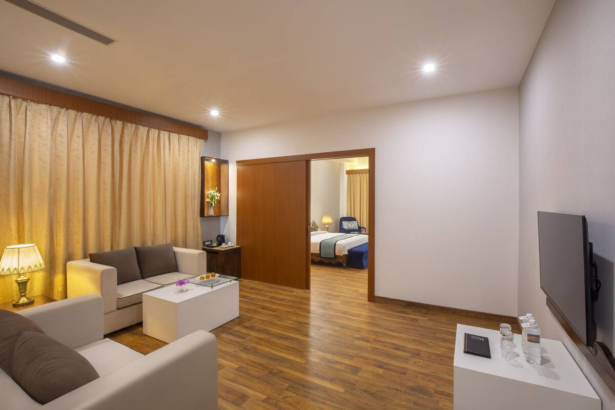 A modern hotel room with a sofa, coffee table, TV, and a wooden floor.