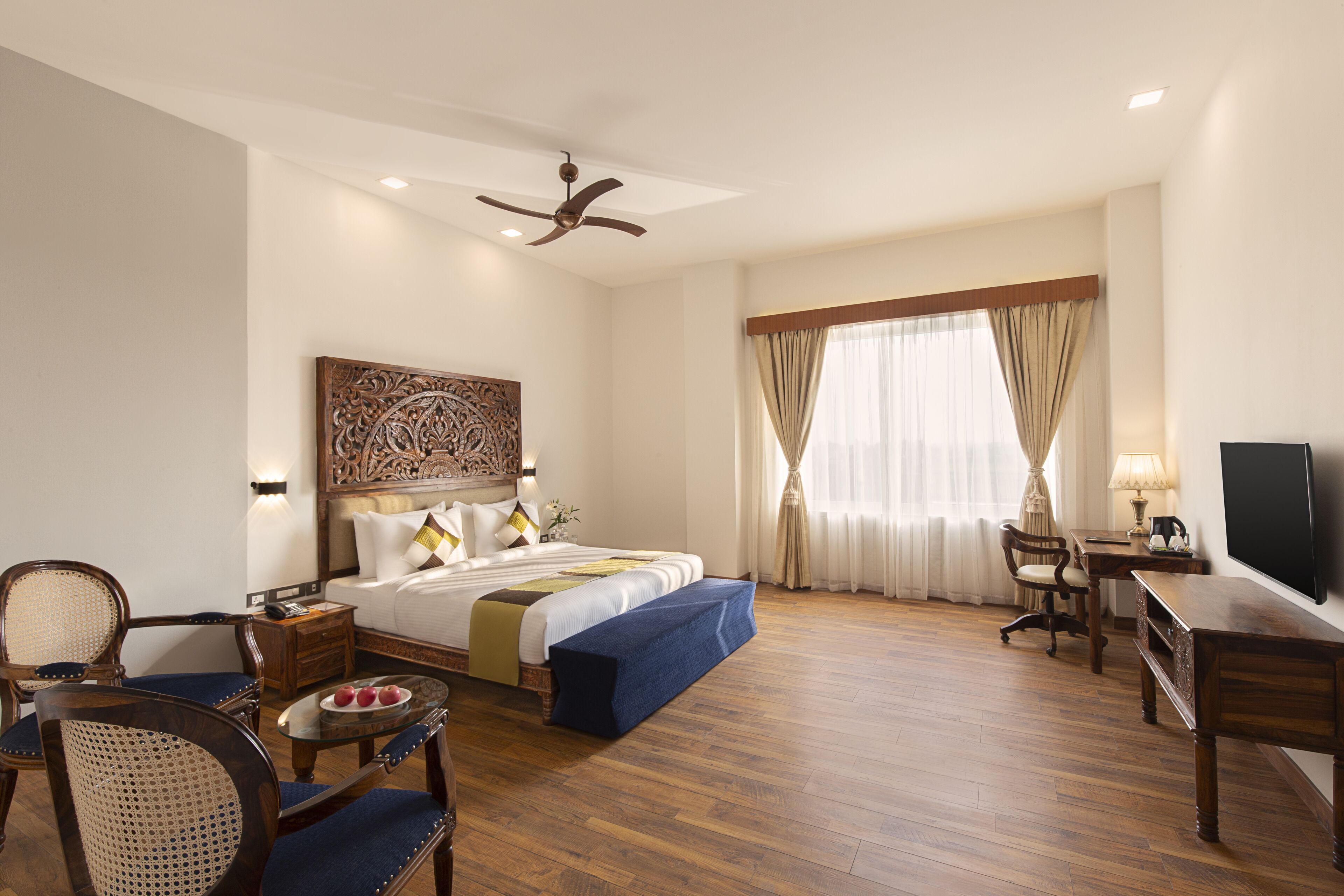 A hotel room with a bed, a desk, a chair, a television, and a ceiling fan.